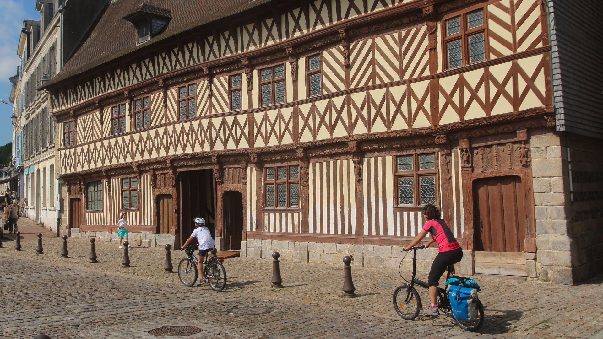 2 vélos passent devant une façade à colombage en Normandie