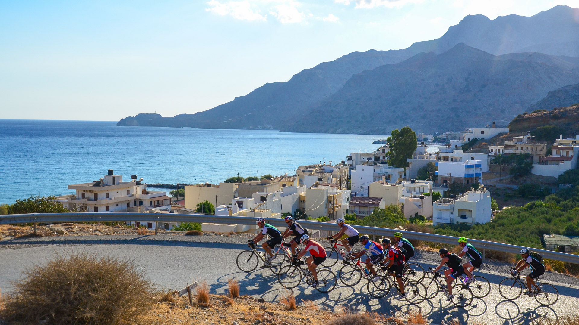 groupe de cyclistes qui descendent une route en balcon, avec la baie de Tsoutsouros en arrière plan