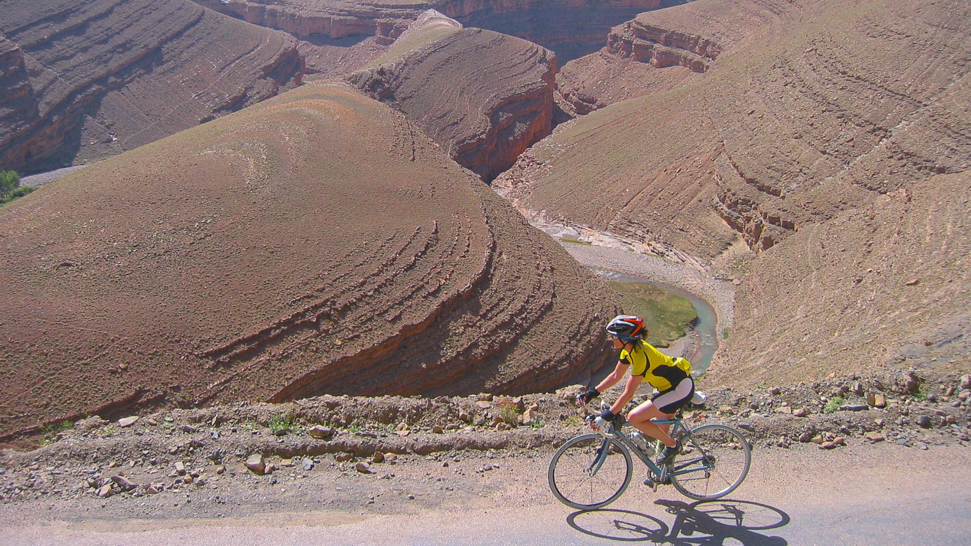 cycliste sur une route en balcon dans le Haut-Atlas, qui surplombe une petite rivière.