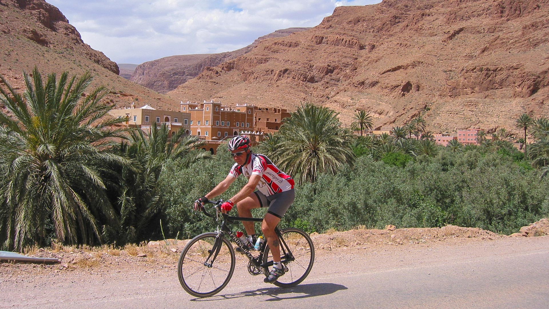 cycliste qui parcourt l'Atlas en vélo de route, avec un village berbère en arrière plan