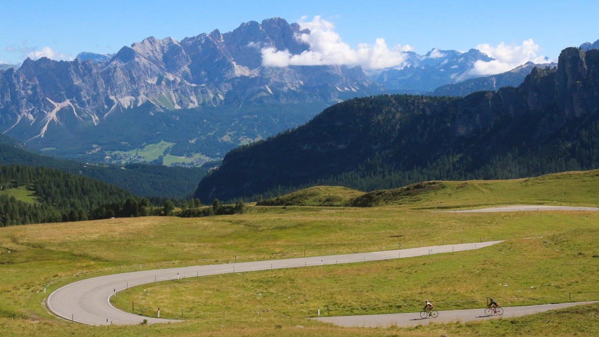 deux cyclistes qui descendent un col dans les Dolomites, avec la vue sur une chaîne de montagne