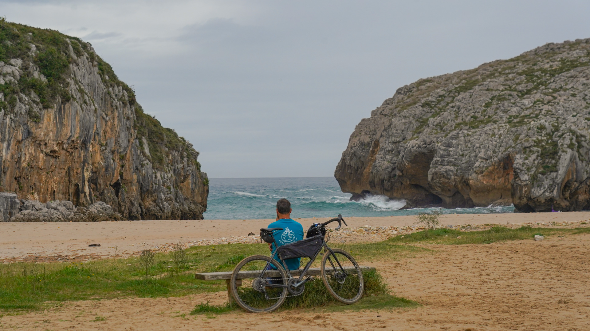 un cycliste de dos assit sur un banc sur la plage Cuevas del Mar, qui regarde la mer et les falaises