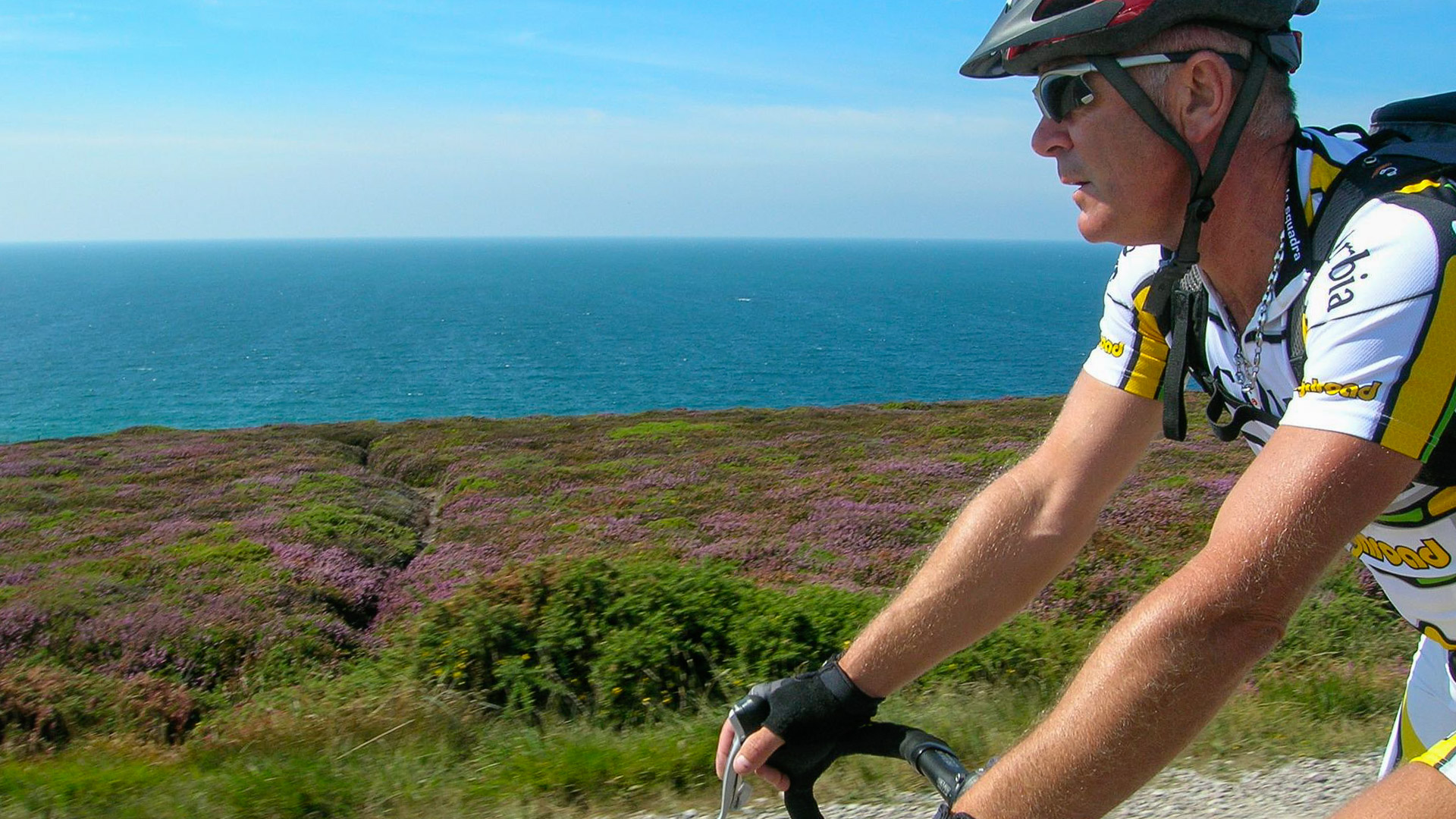 un cycliste qui parcourt une route qui longe la côte bretonne, avec la vue sur la mer.