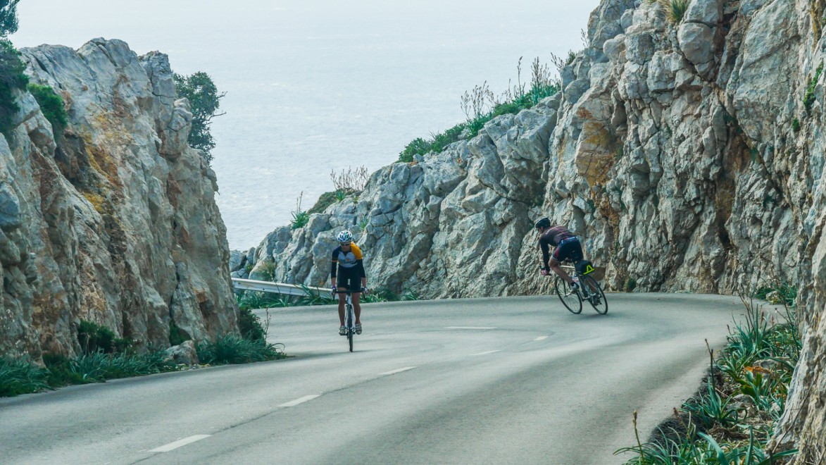 deux cyclistes qui se croisent dans un virage, dans une route côtière