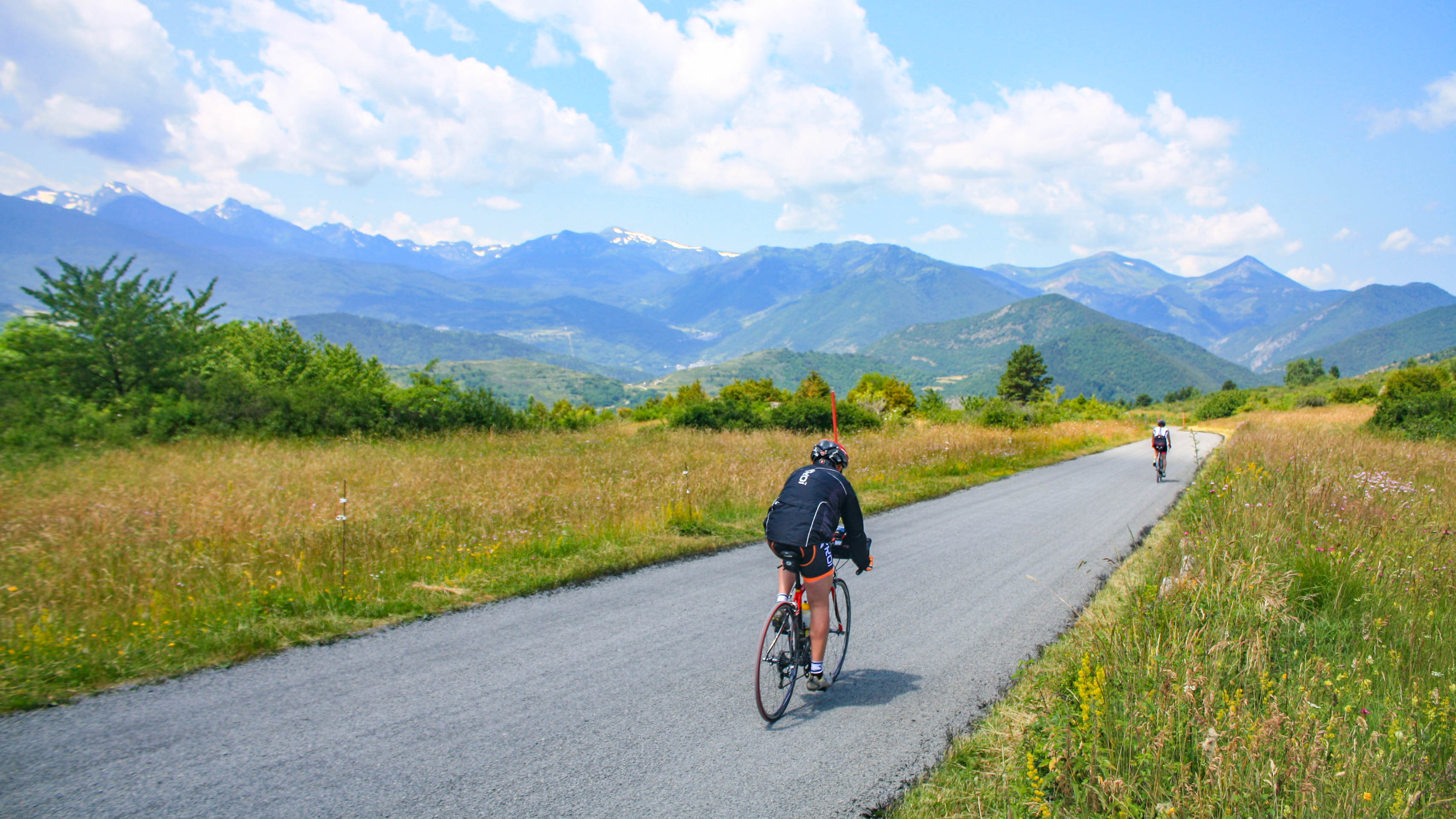 deux cyclistes sur une petite route goudronnée au milieu des champs