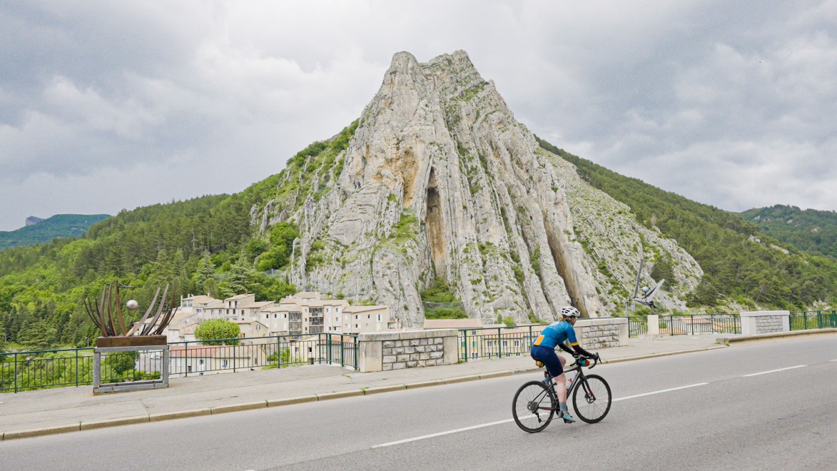 un cycliste qui passe devant la citadelle fortifiée de Sisteron, située au pied du Rocher de la Baume
