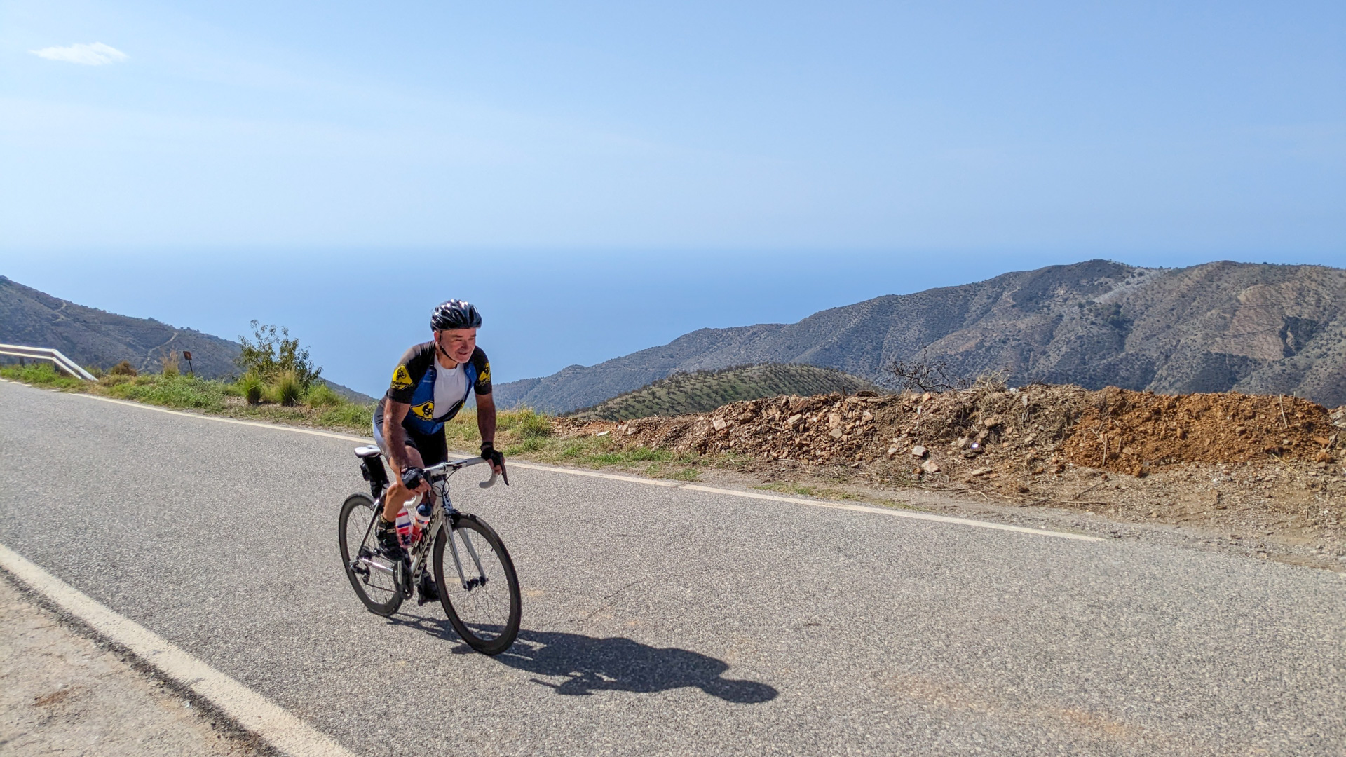 cycliste en danseuse qui monte un col, avec en arrière plan la vue sur la mer Méditerranée