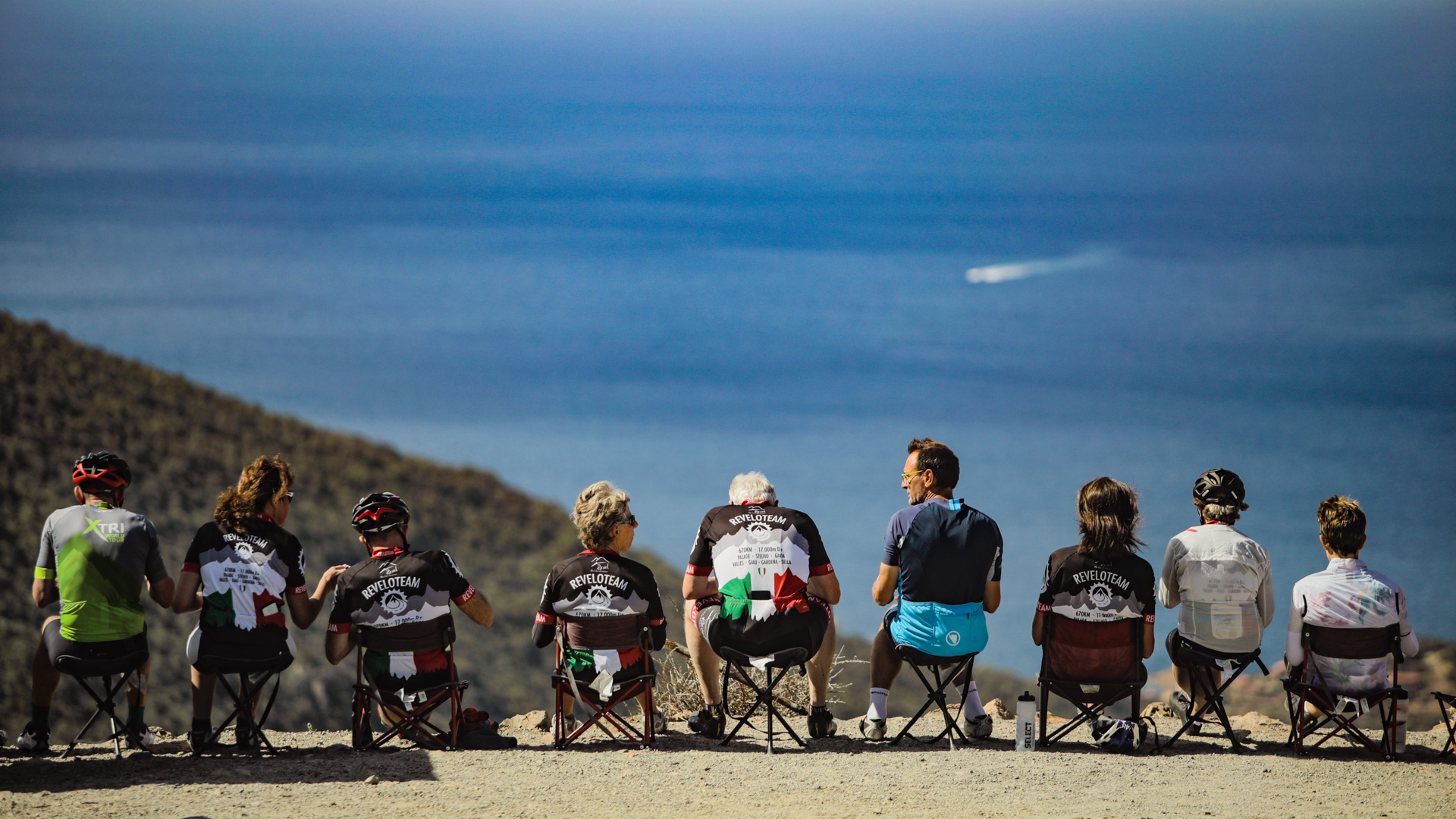 groupe de cyclistes assis, qui pique-nique en altitude face à la mer