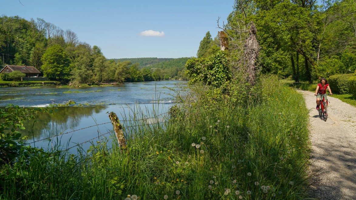 Femme à vélo sur une petite route qui longe une rivière