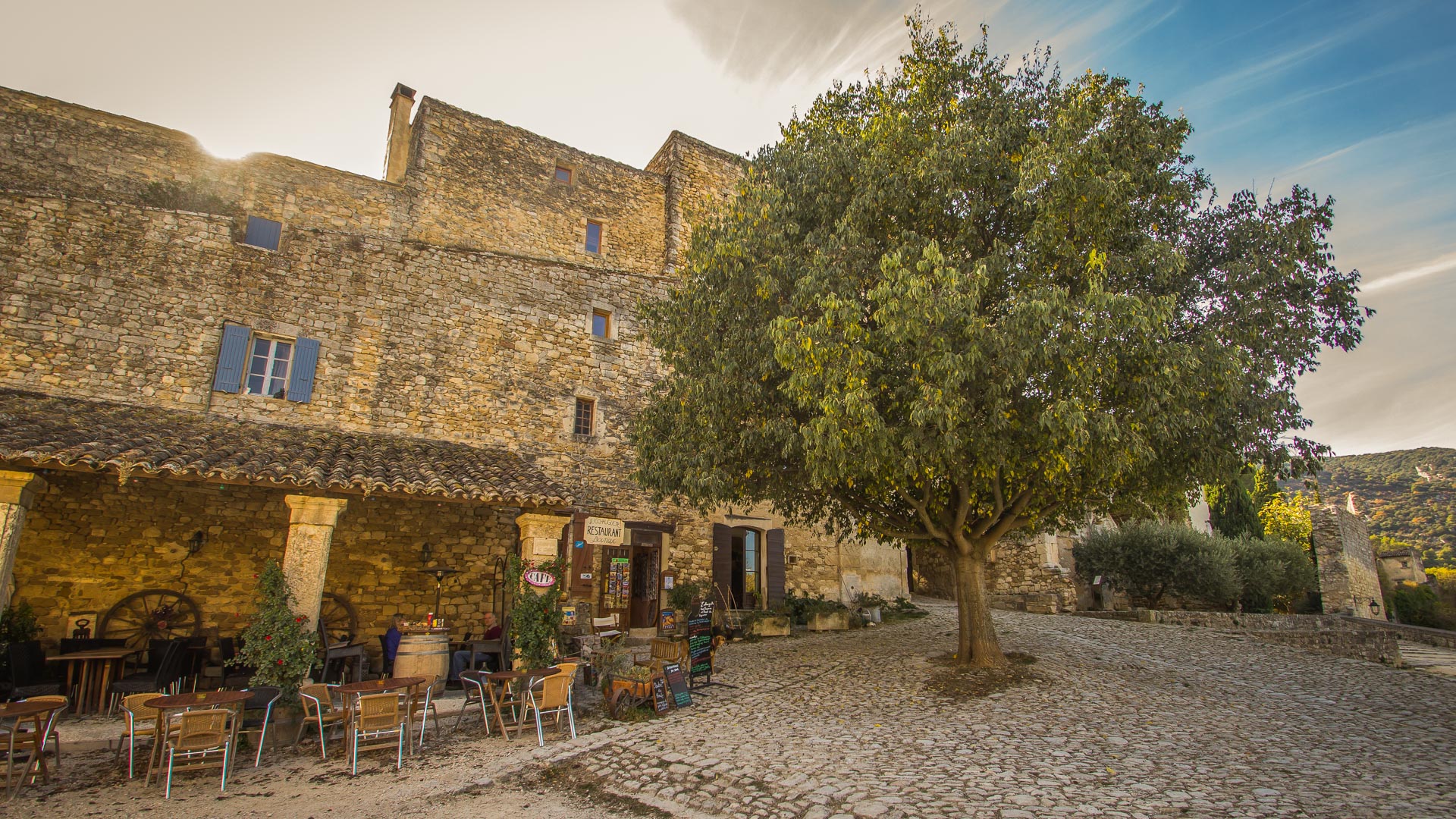 coucher du soleil sur une place d'un village typique du Luberon, avec les habitations en pierre
