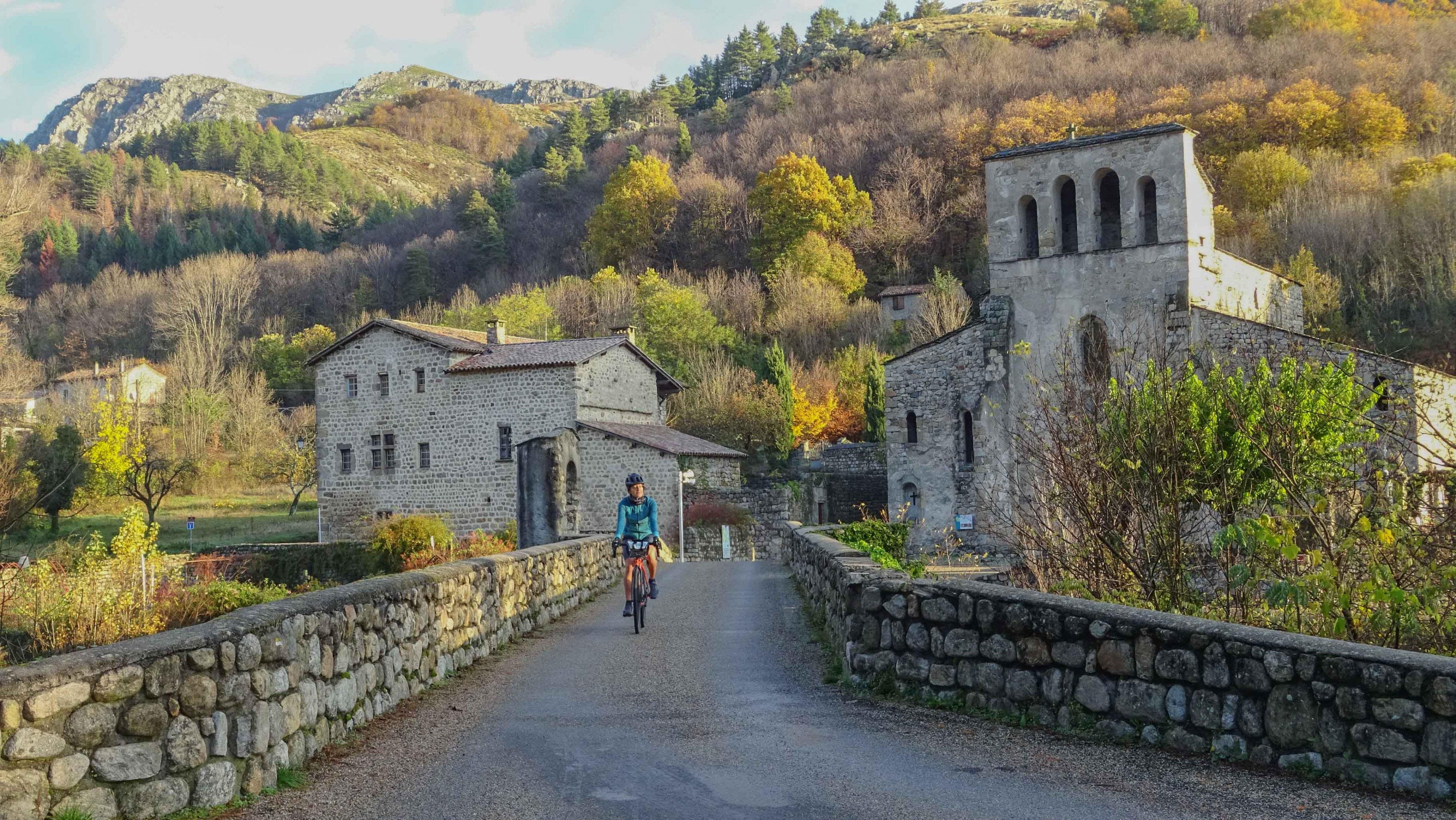 traversée d'une cycliste sur un pont, devant  l'Église Notre-Dame de ¨Prévenchères, à Montpezat-sous-Bauzon