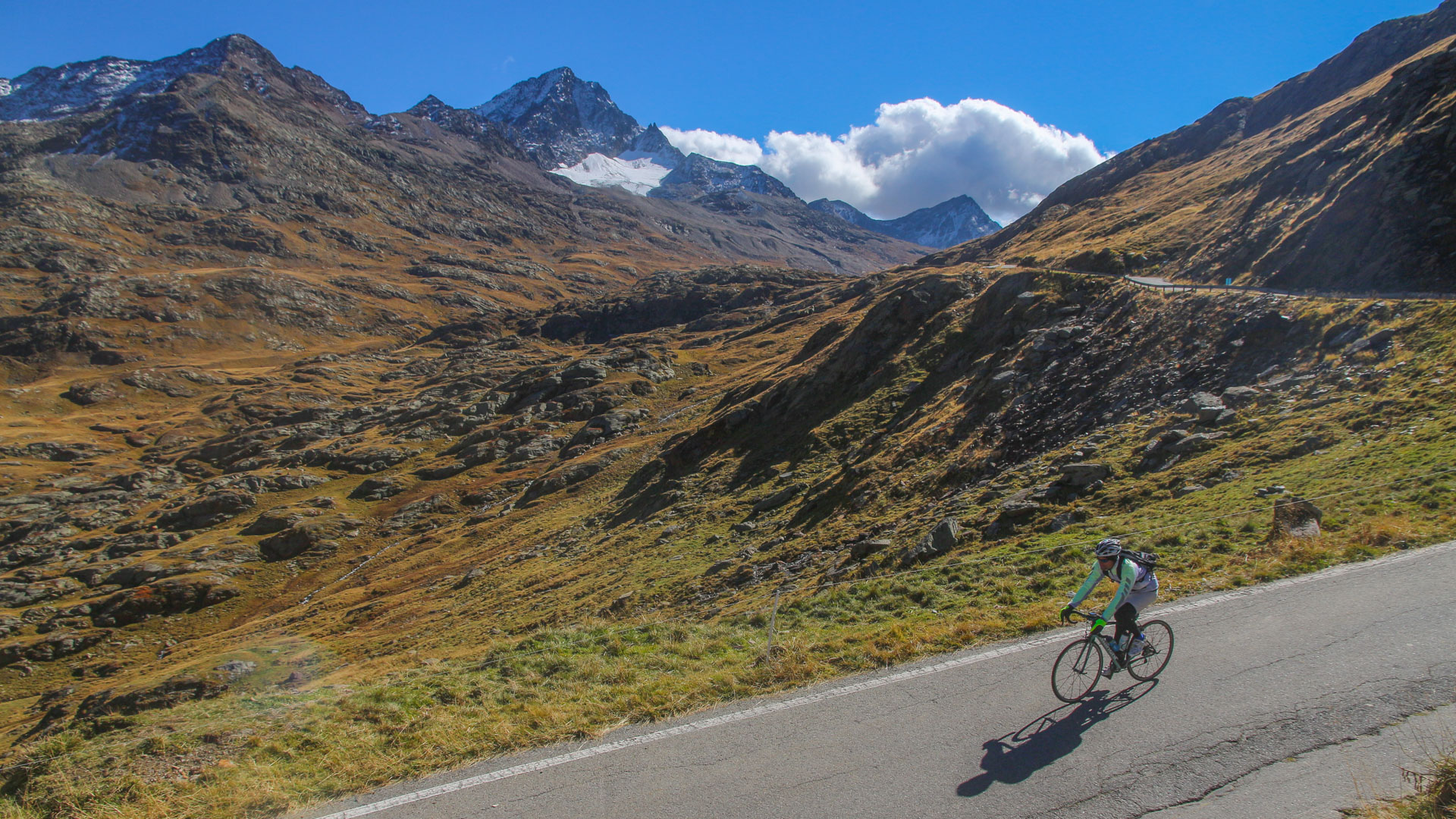 un cycliste qui descend une route en pleine montagne, avec un glacier en toile de fond