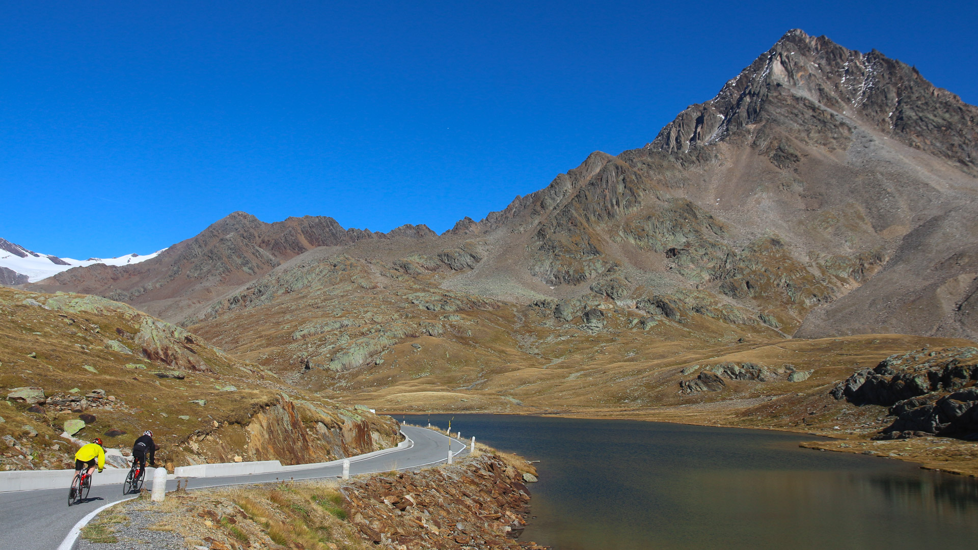 cyclistes qui font l'ascension du col du Gavia, dans les Alpes italiennes, avec la route qui passe au bord du lac Blanc