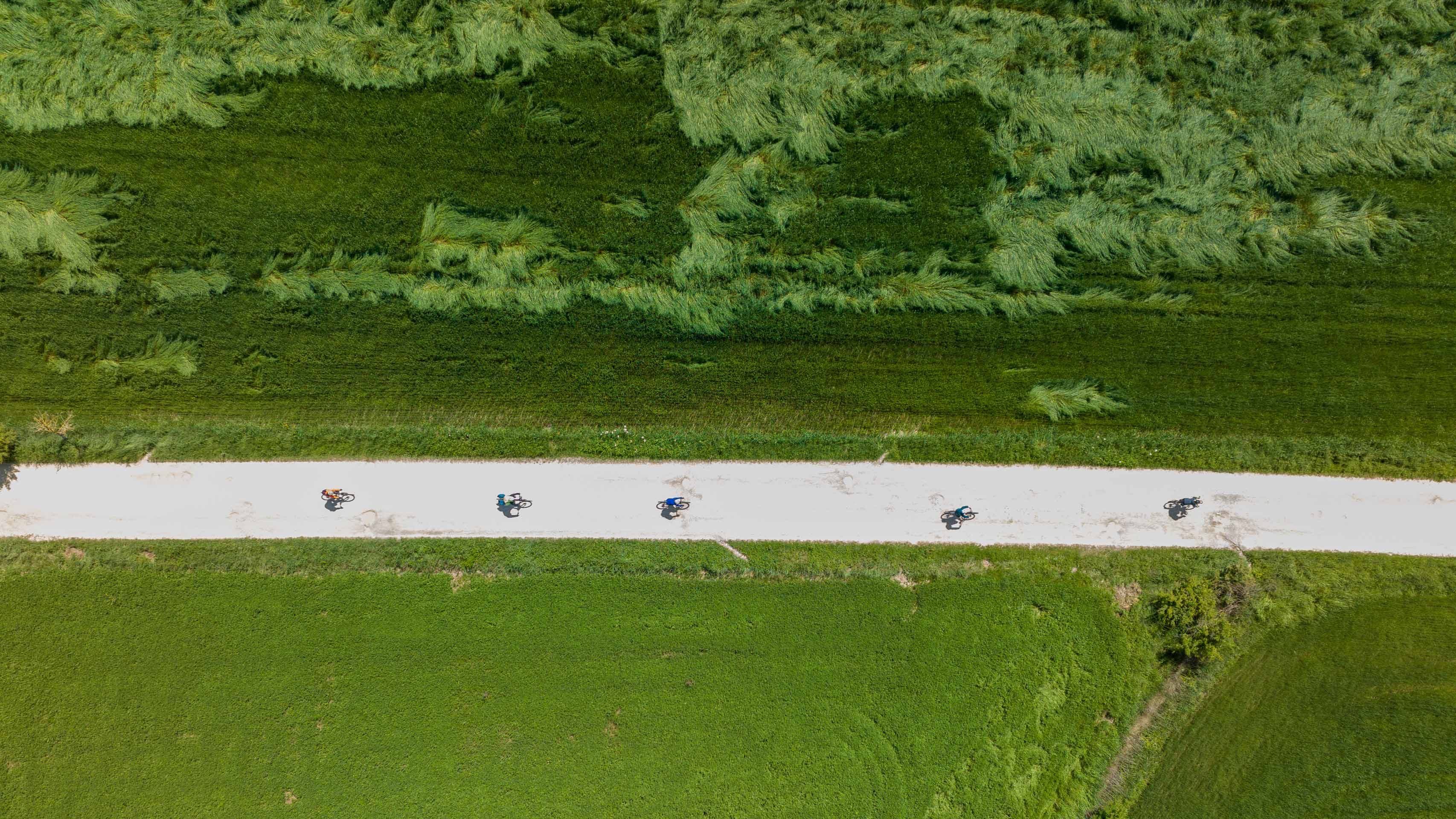 vue aérienne sur des cyclistes gravel parcourant une piste blanche à travers les champs de la Toscane