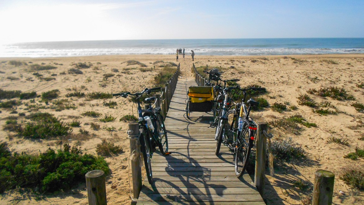 vélos et remorques enfant parqués sur une passerelle en bois vers une plage portuguaise
