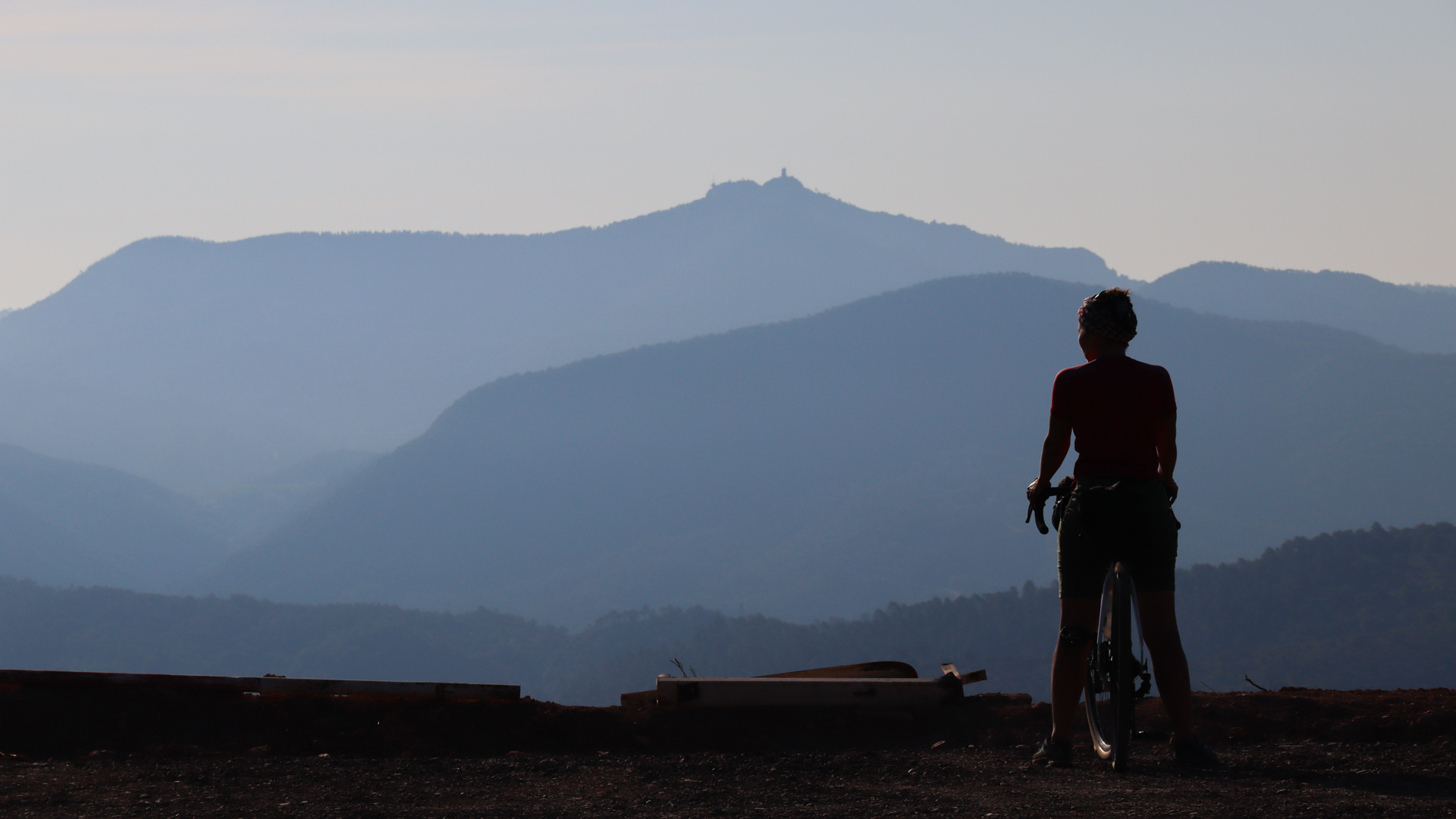 une cycliste de dos à l'arrêt, observant le paysage et le Mont Ventoux en fin de journée