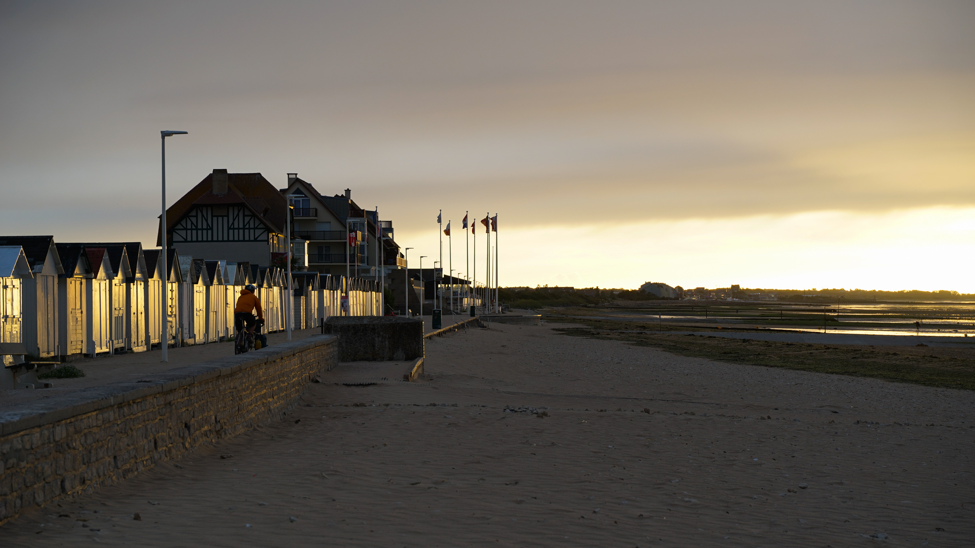 cycliste dans la lumière du soir, devant les cabines de plage de Normandie