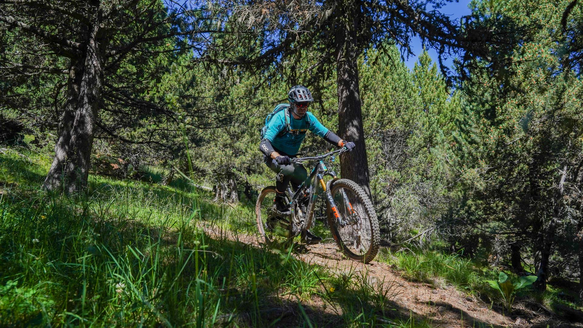 un VTT monte sur un sentier à travers les pâturages avec une falaise en toile de fond