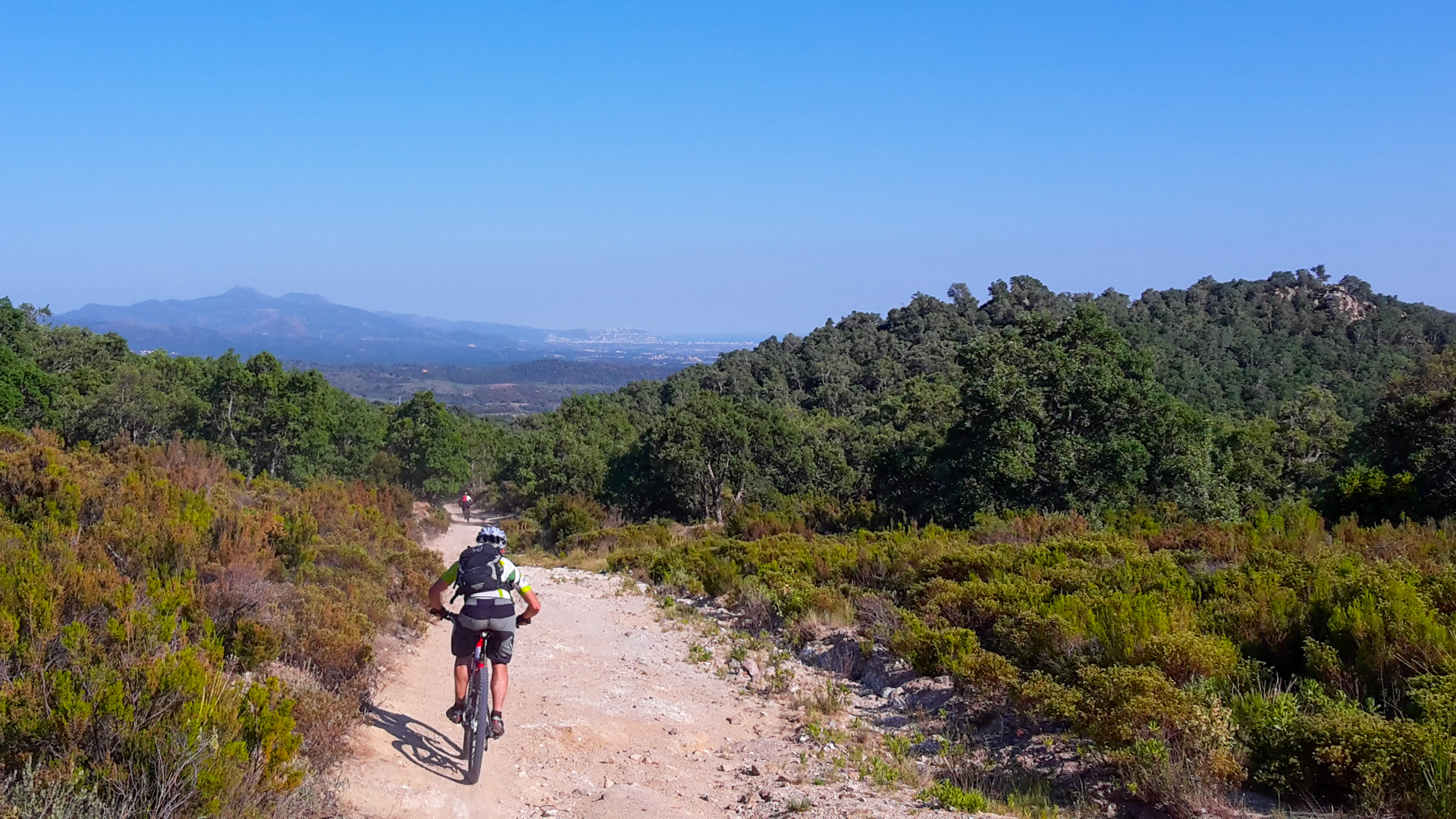 homme à vtt descend une piste tête dans le guidon en direction de la mer