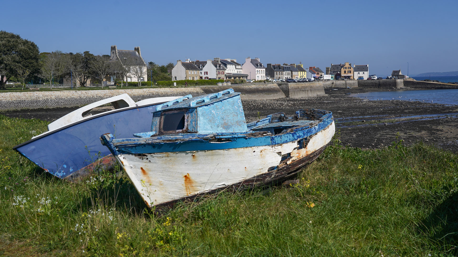 des bateaux échoués sur une plage à marée basse avec un petit village breton en fond
