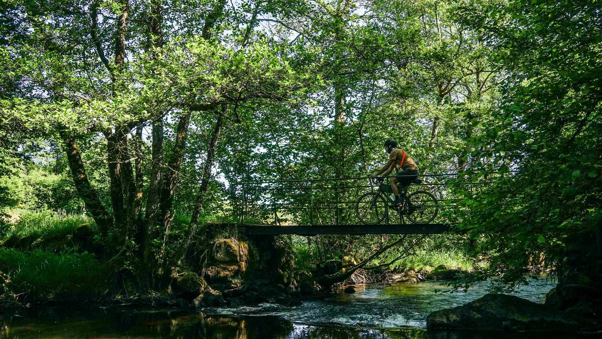 cycliste gravel passe à vélo sur une passerelle au dessus de la rivière