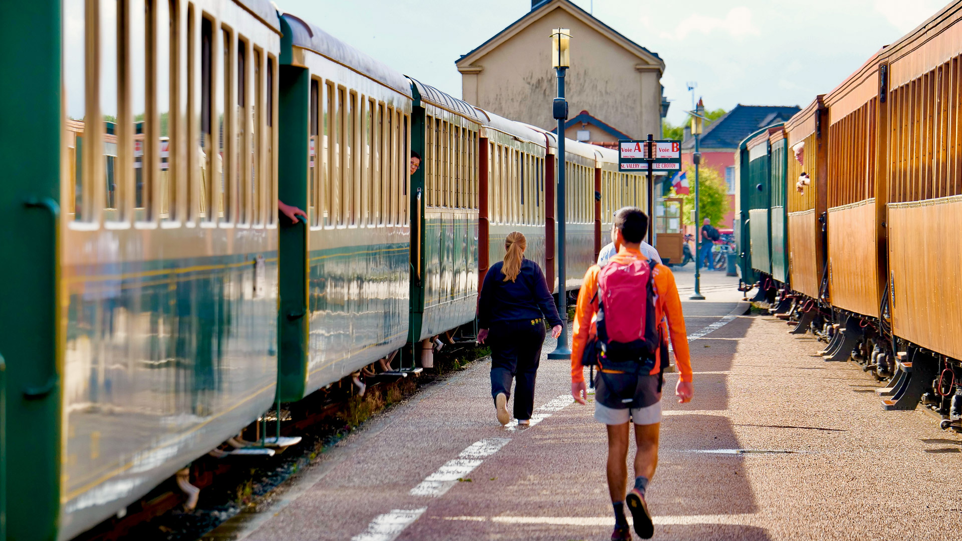 on voit 3 piétons au centre de l'image, encadrés par deux trains, desquels des personnes commencent à sortir