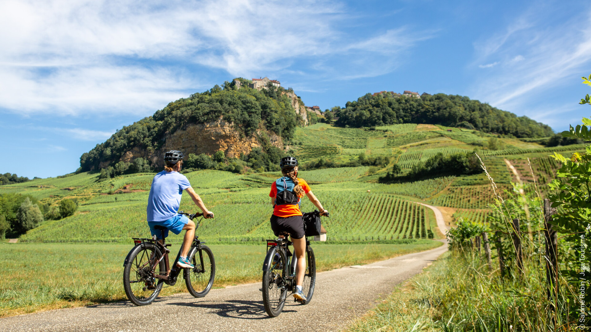 Couple en vacances à vélo sur une petite route entourée de vignes à proximité de Château-Chalon