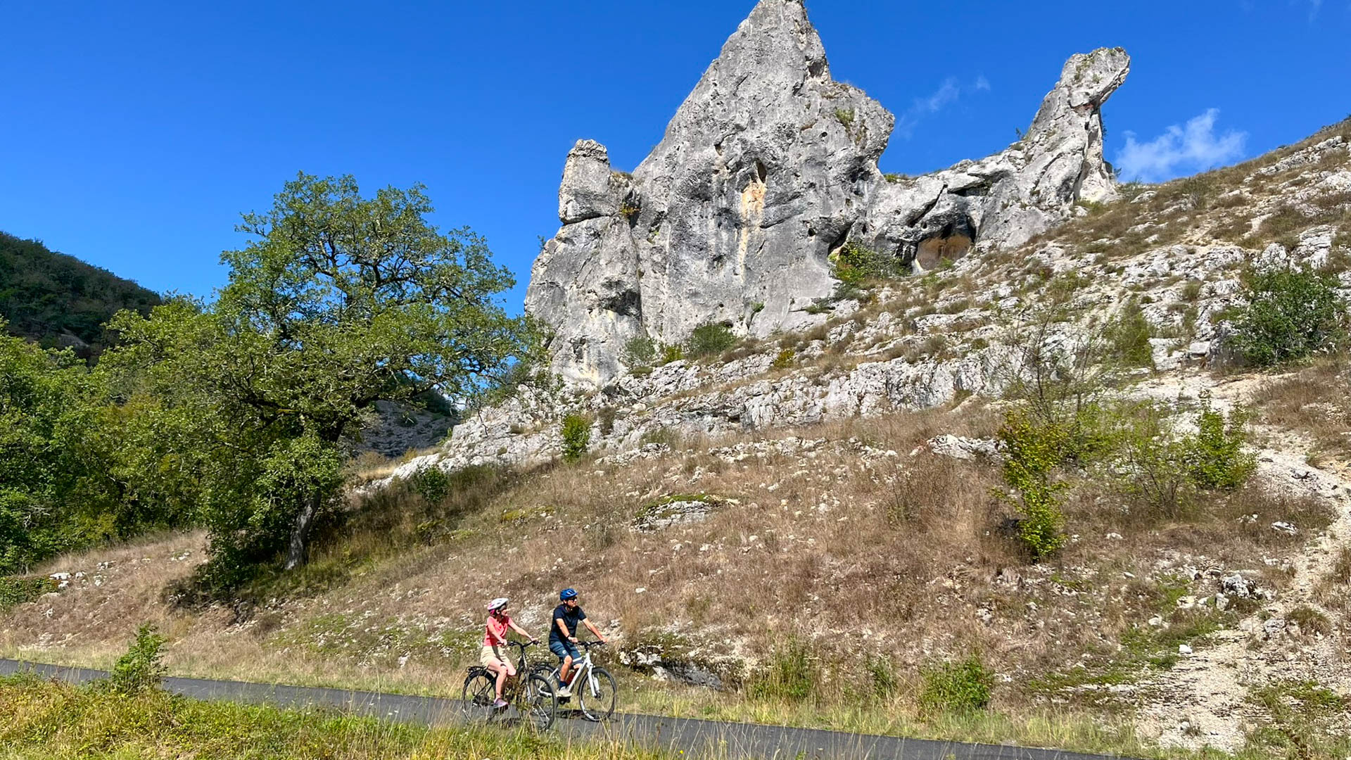 couple à vélo sur une petite route bordée de monolithes rocheux dans le parc des causses du Quercy