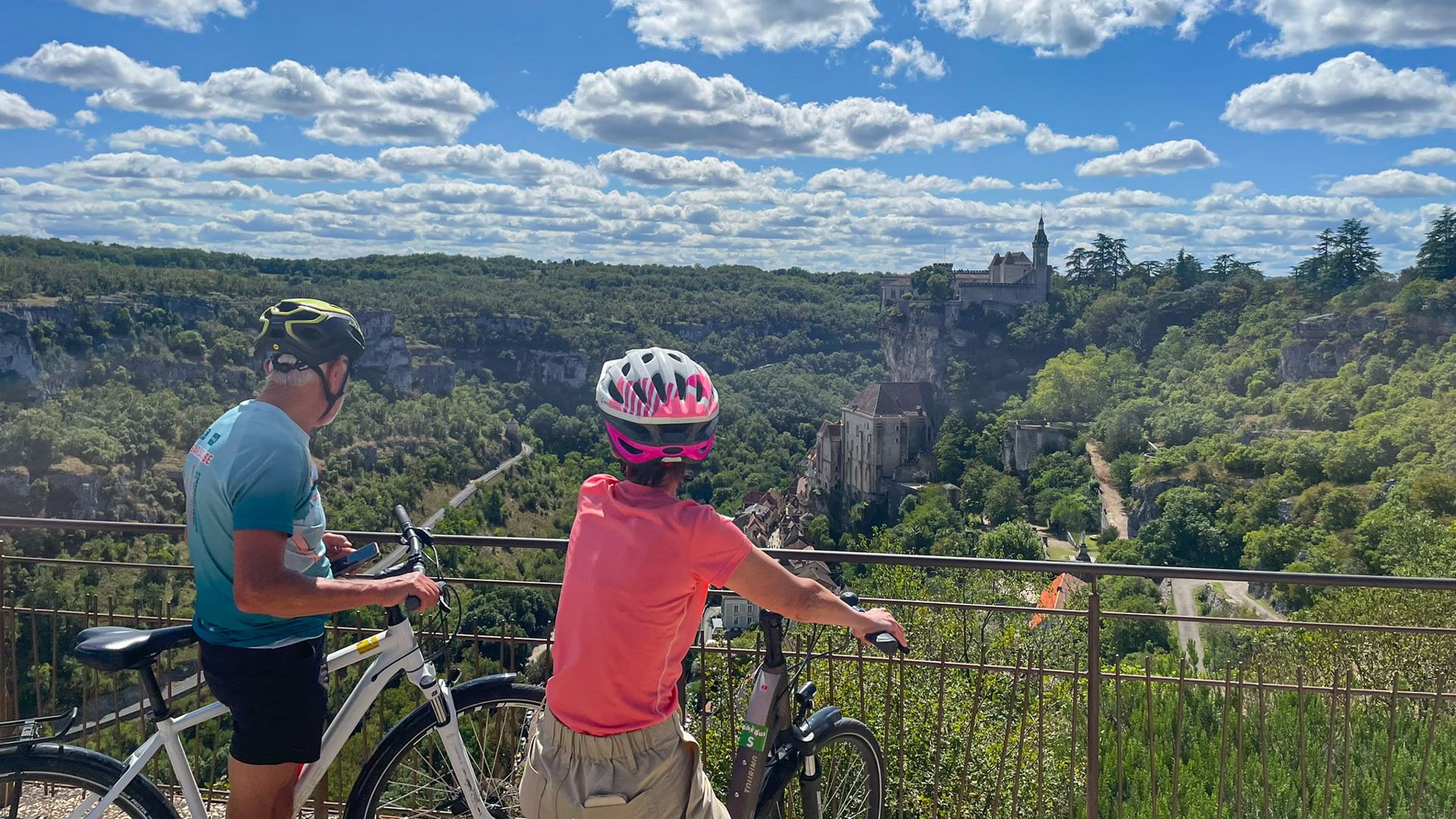 Couple à vélo admire le village perché de Saint-Cirq-Lapopie dans le Lot