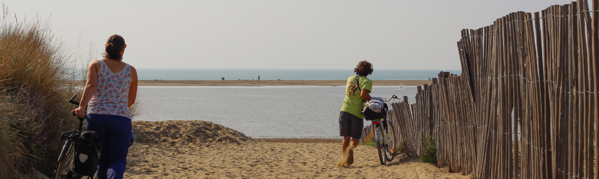 deux voyageurs vélo poussent leurs vélo dans le sable en arrivant à la mer